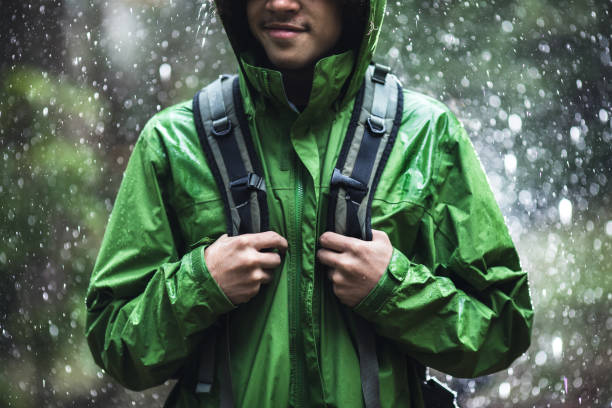 A young adult African American man goes for a hike in the rain in Pacific Northwest, the raindrops repelling from his raincoat.